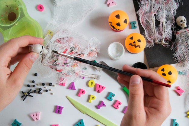 Children's hands paint on the bandage with paint. Paper, bandage, plasticine with paints on a wooden table. Halloween postcard spider and cobweb, ghostly skeletons. Crafts for children