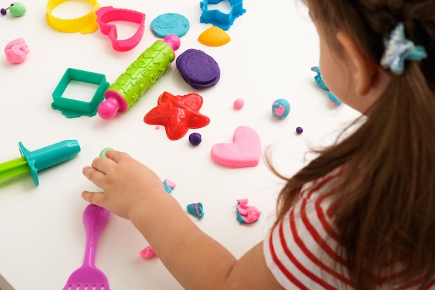 Children's hands with multicolored plasticine and molds on white table little girl made plasticine pink heart