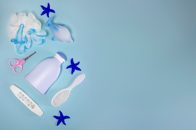 Children's hygiene: bath items, shampoo bottle, rubber toy, sponge, comb, thermometer, safety scissors top view, on a blue background. copy space. Children's personal care kit. Bath accessories.