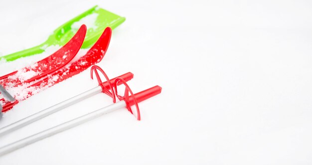 Children's red skis with sticks and a green snow shovel-layout in the snow