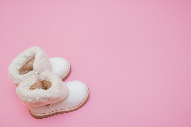 Children's white fur boots on a pink background with copy space