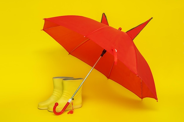 Children's yellow rubber boots under a red children's umbrella on a yellow background