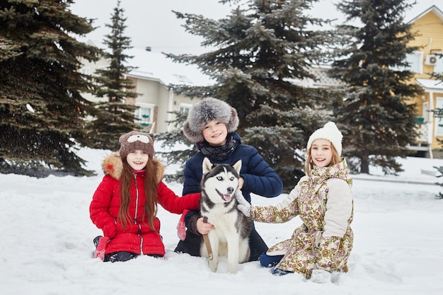 Children sit in the snow and stroked dog husky. Children go out and play with husky dog in winter. Walk in the Park in winter, joy and fun, dog husky with blue eyes. Russia, Sverdlovsk, 28 Dec 2017