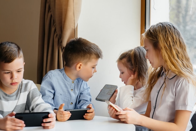 Children sit at table in cafe and play mobile phones together.