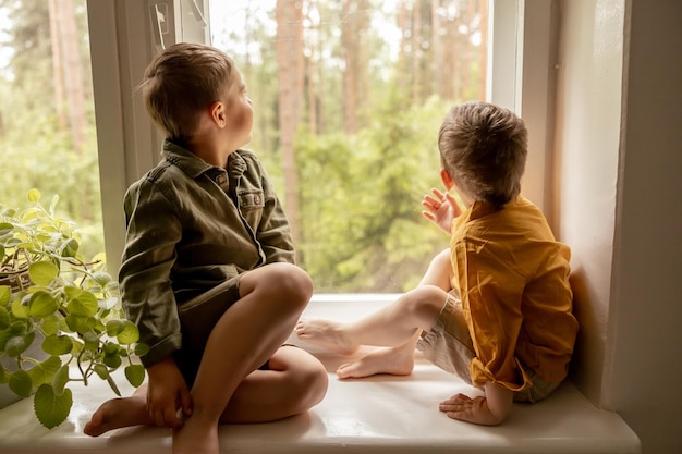 Children sitting on windowsill and waiting for someone comming Two brothers friends Cute preschool kids alone at home Boys are waiting for their mother or father Loneliness Busy parents