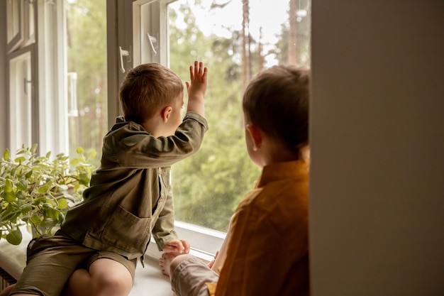 Children sitting on windowsill and waiting for someone comming Two brothers friends Cute preschool kids alone at home Boys are waiting for their mother or father Loneliness Busy parents