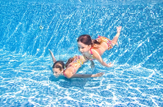 Children swim in swimming pool underwater little active girls have fun under water kids fitness