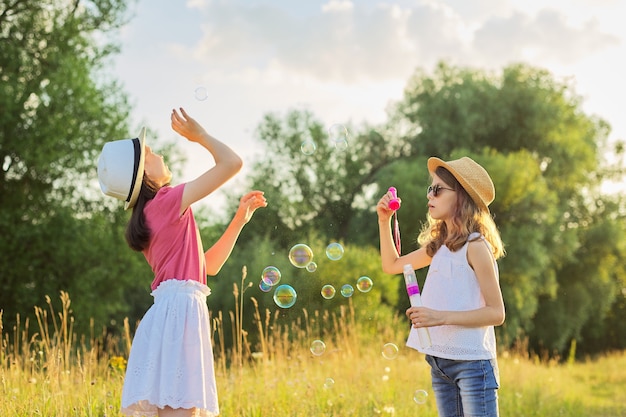 Children two girls blowing soap bubbles. Beautiful natural landscape, summer meadow background, happy childhood