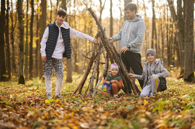 Children with father constructs a house from sticks in autumn forest