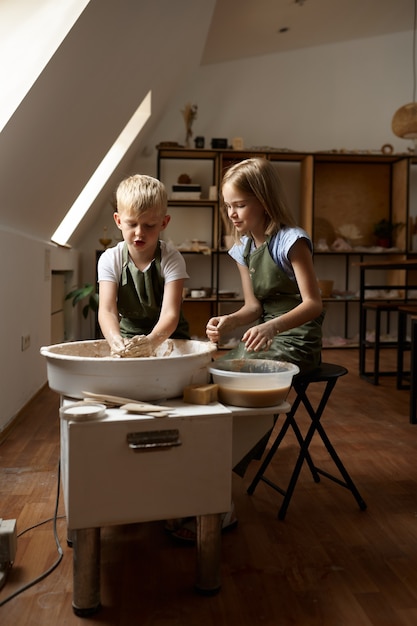 Children work on a potter's wheel in the workshop. Clay modeling lesson at the art school. Young masters of folk crafts, pleasant hobby, happy childhood