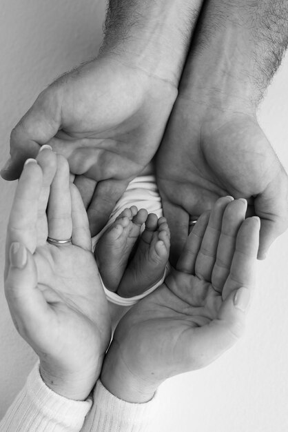 Children39s leg in the hands of mother father parents Feet of a tiny newborn close up Little baby foot Mom and her child Happy family concept Black and white photo of motherhood