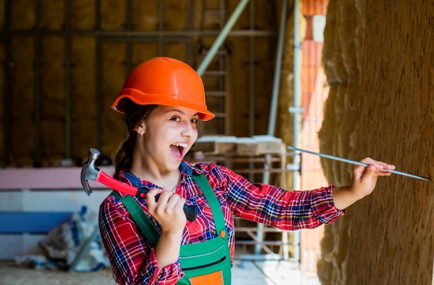 Childrens creativity kid wear helmet on construction site teen girl builder with building tool hammer child on repairing work concept of renovation in workshop busy professional carpenter