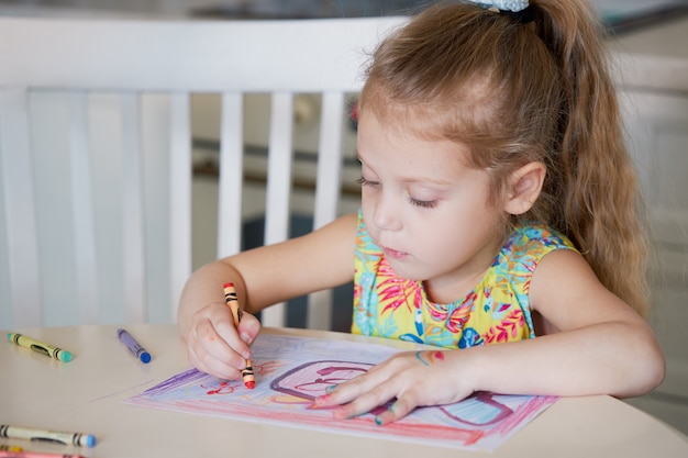 Childrens creativity. Little child girl draws with wax pencils at home. The concept of distance learning online for the period of global quarantine.