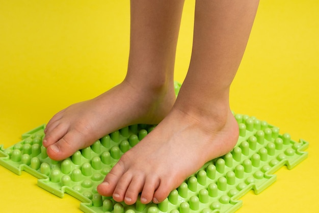 Childrens feet on a green orthopedic mat on a yellow background treatment and prevention of flat