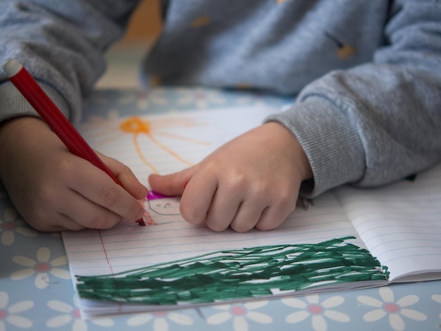 Childrens hands draw with a felttip pen girl sits at the table and draws