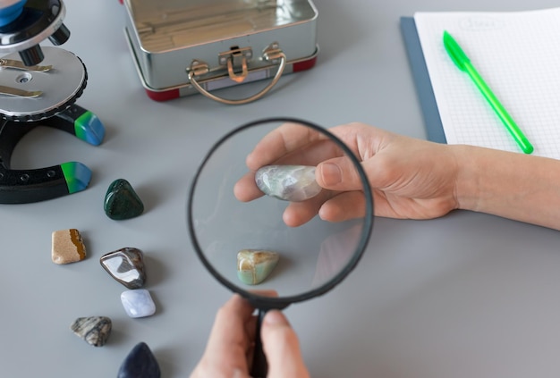 Childrens hands holding magnifying glass and studying semiprecious stones at school lesson