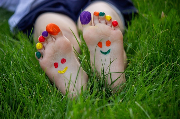 Childrens legs with a pattern made of paints are smiling on the green grass