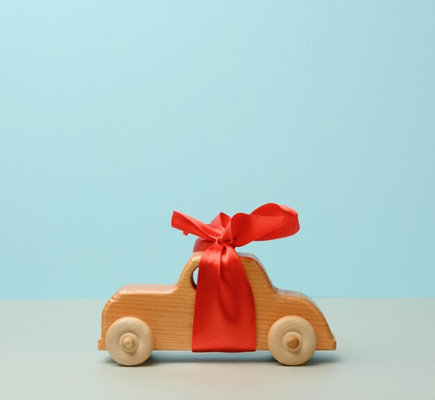 Photo childrens wooden toy car with a red bow on a blue background the concept of buying a car a p