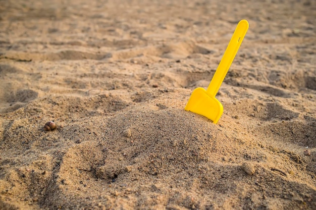 Childrens yellow shovel stuck in a pile of sand on the beach