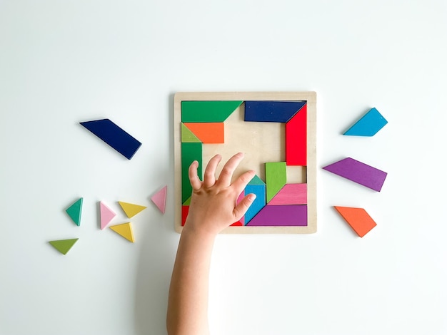 Childs hand collects multicolored wooden mosaic on white background child solves colorful tangram