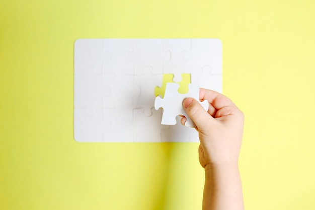 Childs hand holding the last piece of white puzzle on yellow table