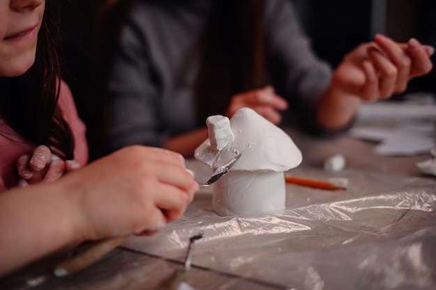 Photo a childs hands construct a clay house with the focused guidance of a parent symbolizing the joy