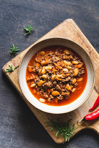 Chili Con Carne in bowl on dark background Mexican cuisine chili con carne minced meat and vegetables stew in tomato sauce Top view