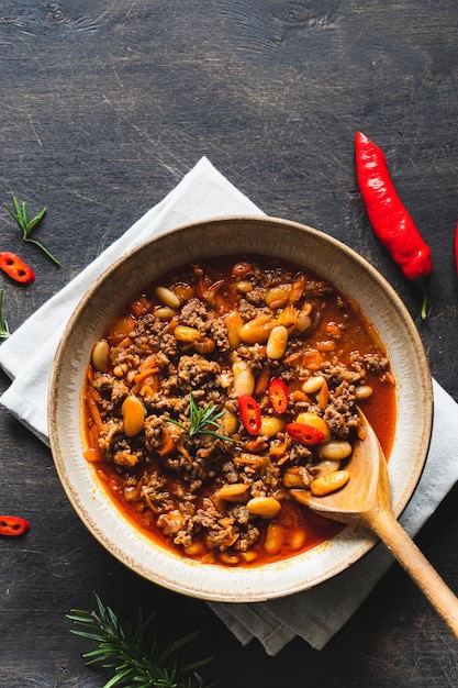 Chili Con Carne in bowl on dark background Mexican cuisine chili con carne minced meat and vegetables stew in tomato sauce Top view