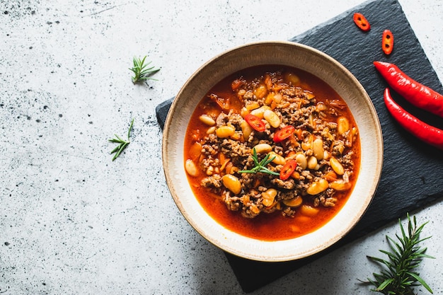 Chili Con Carne in bowl on light grey stone or concrete background Mexican cuisine chili con carne minced meat and vegetables stew in tomato sauce Top view