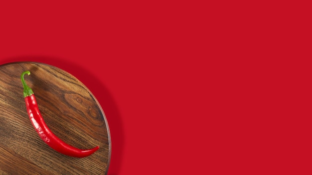 Chili pepper on a wooden board The board is located in the lower left corner on a red background