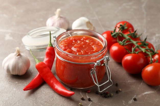 Chili sauce in glass jar and ingredients on grey, close up