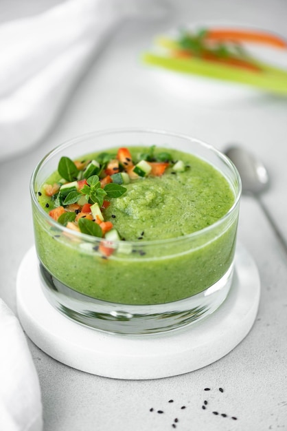 Chilled cucumber gazpacho with tomato pieces and basil in a glass bowl closeup