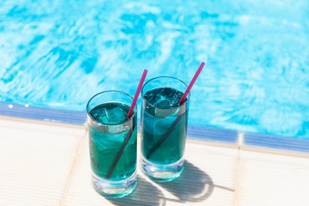 Chilled soft drinks two blue cocktails with ice near the swimming pool in sunny day