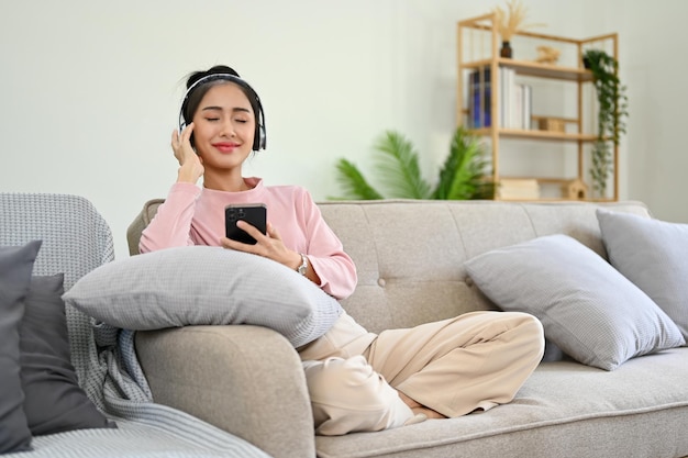 Chilling and relaxing Asian female on sofa listening to music through her headphones