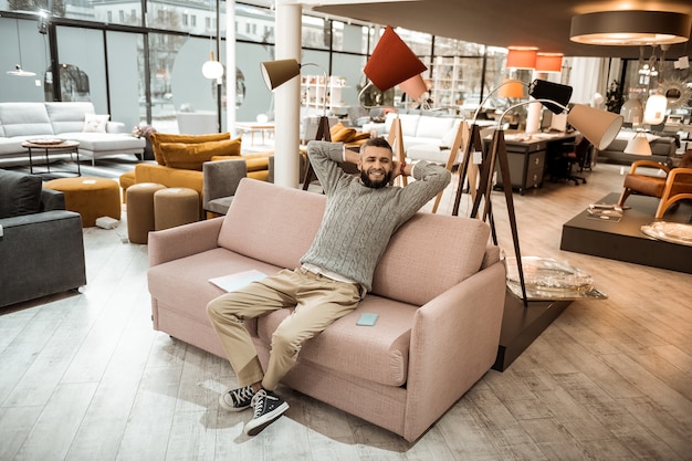 Photo chilling on sofa. smiling man in grey sweater resting on the sofa in the middle of the furniture store