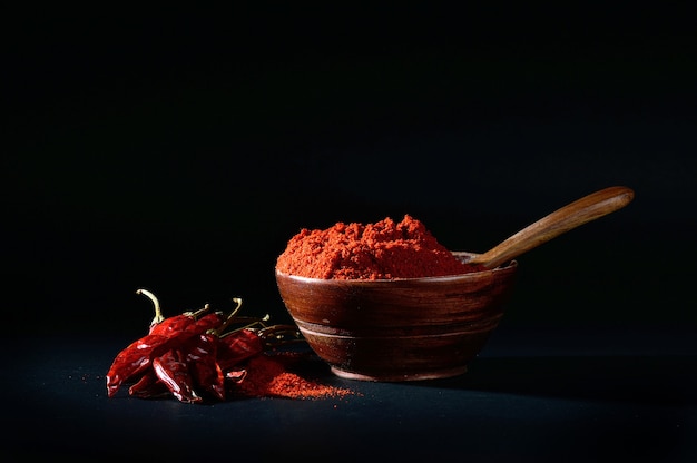 Chilly powder in wooden bowl with red chilly, dried chillies on black