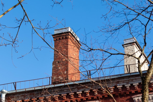 Chimney of old red brick house against blue sky and tree branches