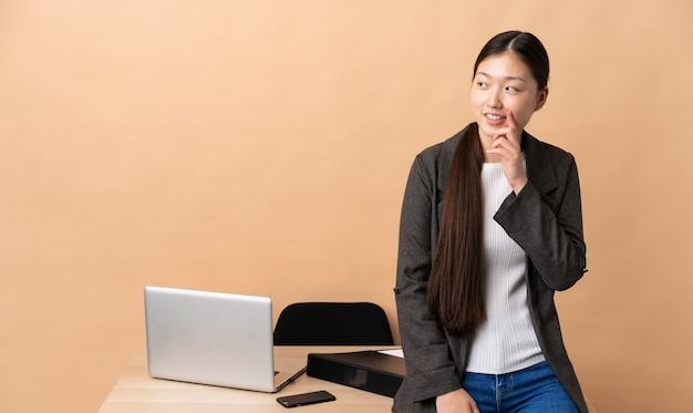 Chinese business woman in her workplace thinking an idea while looking up