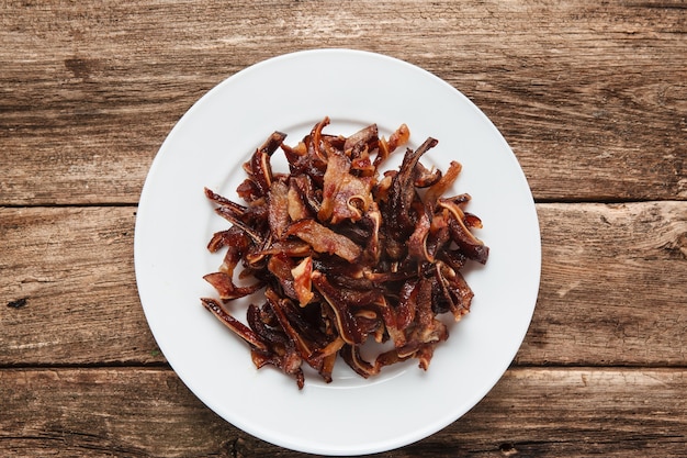 Chinese food, tasty beer snacks. Smoked spicy pig ears served on white plate, on rustic wooden table. Top view.