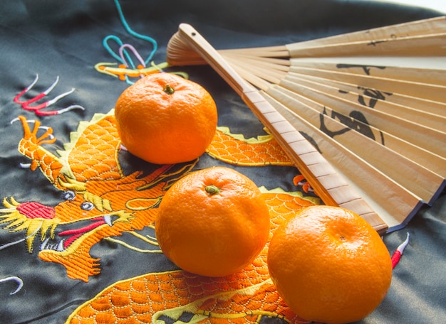 Photo chinese new year, tangerines and a fan lying on the silk fabric with an embroidered dragon