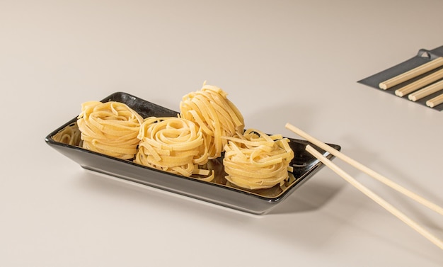 Chinese noodles on a black plate and bamboo chopsticks