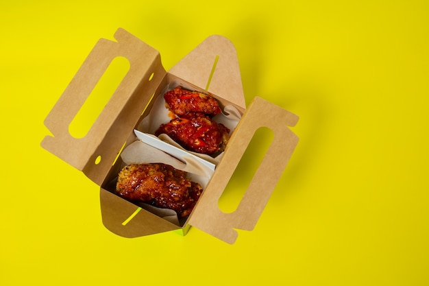 Chinese takeaway chicken with tomatoes in a cardboard box photographed on a yellow background