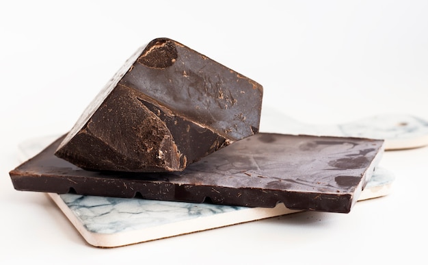 A chipped piece of chocolate with a dark chocolate bar on a light marble board.