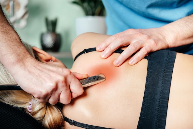 Chiropractor performing myofascial release techniques with IASTM tool for the Rhomboid muscle to relieve scapular pain