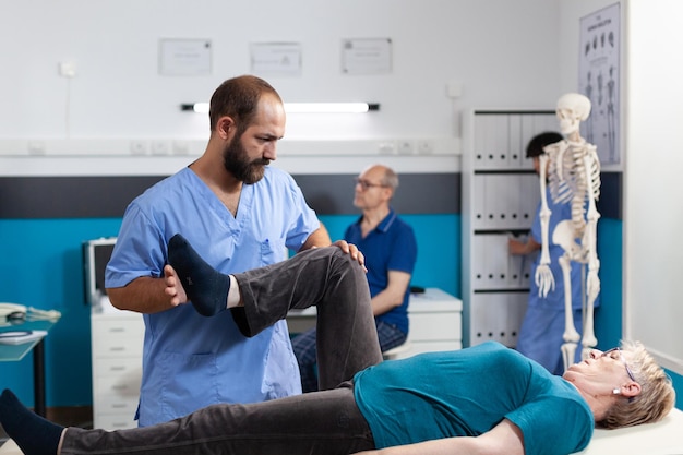 Chiropractor stretching leg muscle to relieve pressure for recovery of retired woman. Medical assistant helping aged patient with knee pain, doing physical exercise for physiotherapy