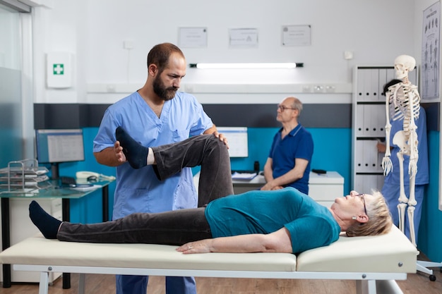 Chiropractor stretching leg muscle to relieve pressure for recovery of retired woman. Medical nurse helping aged patient with knee pain, doing physical exercise for orthopedic care