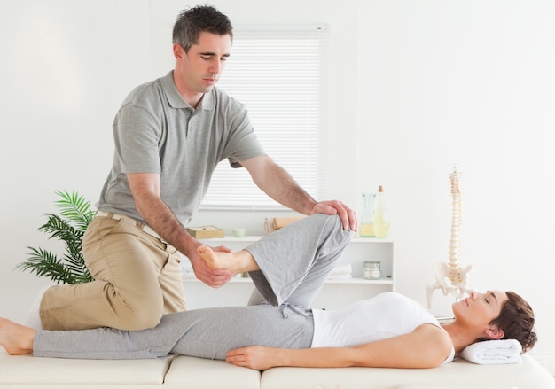 Chiropractor stretching young woman's leg