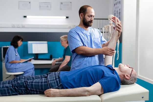 Chiroptractor doing orthopedic massage on aged patient for hand muscle recovery. Nurse helping with physical pain, stretching arm of senior man for osteopathy treatment and healthcare.