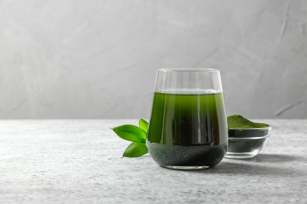 Chlorella healthy detox drink in glass and powder in bowl on a grey space