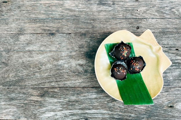 Choc balls or chocolate balls topping with multicolored rainbow sprinkles and colored sugar flower in yellow ceramic dish on wooden table